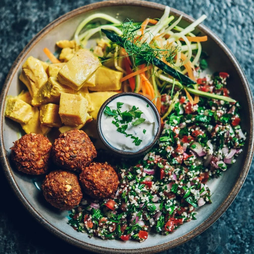 Piletina Garam Masala na tanjiru, sa falafelom, tabule salatom i lebnim sosom.